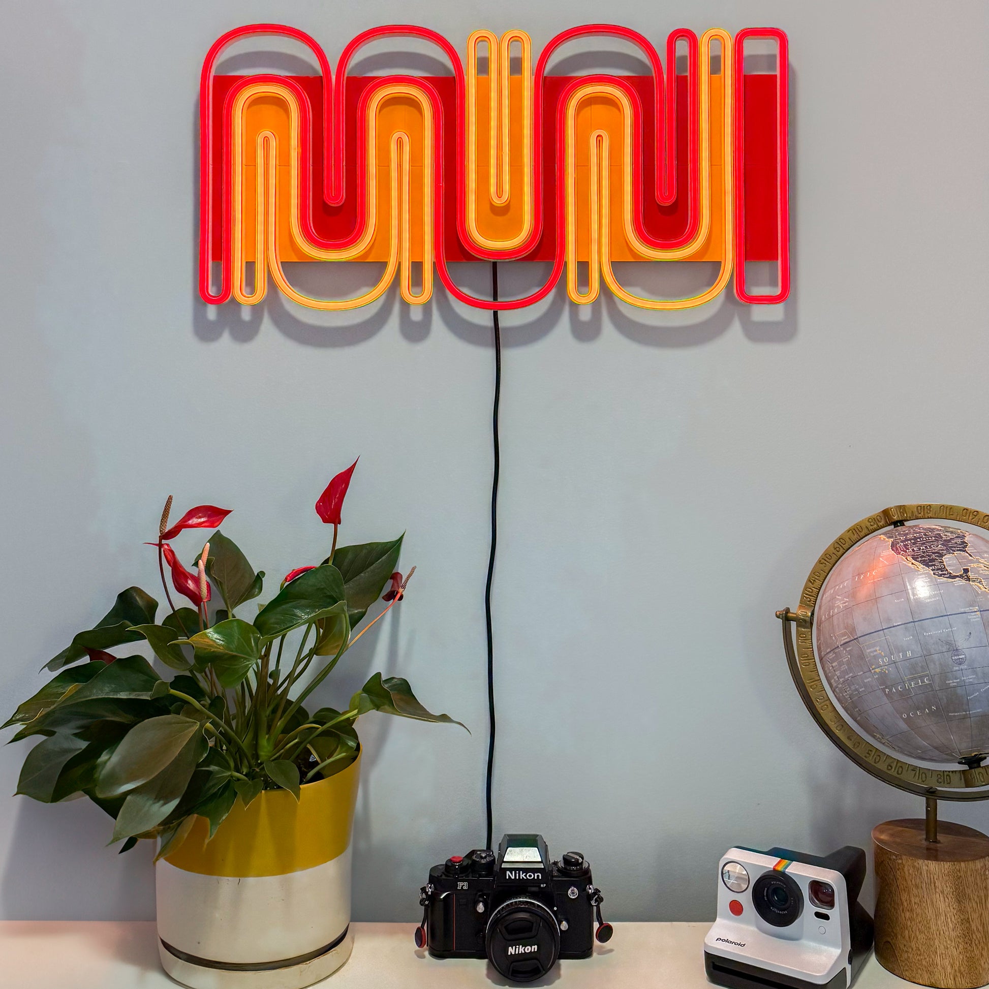 MUNI LED sign handing on a wall above a potted plant, two cameras, and a globe